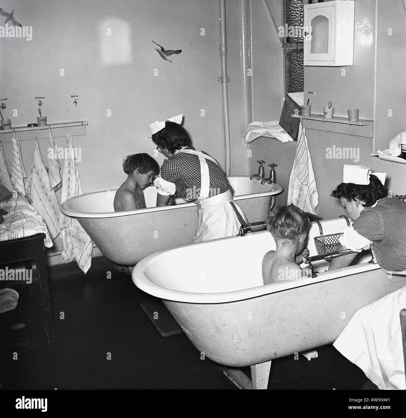 @ Fin des années 40, à un hôpital pour enfants, deux femmes en soins infirmiers, donner aux enfants un bain avant le coucher, England, UK. Banque D'Images
