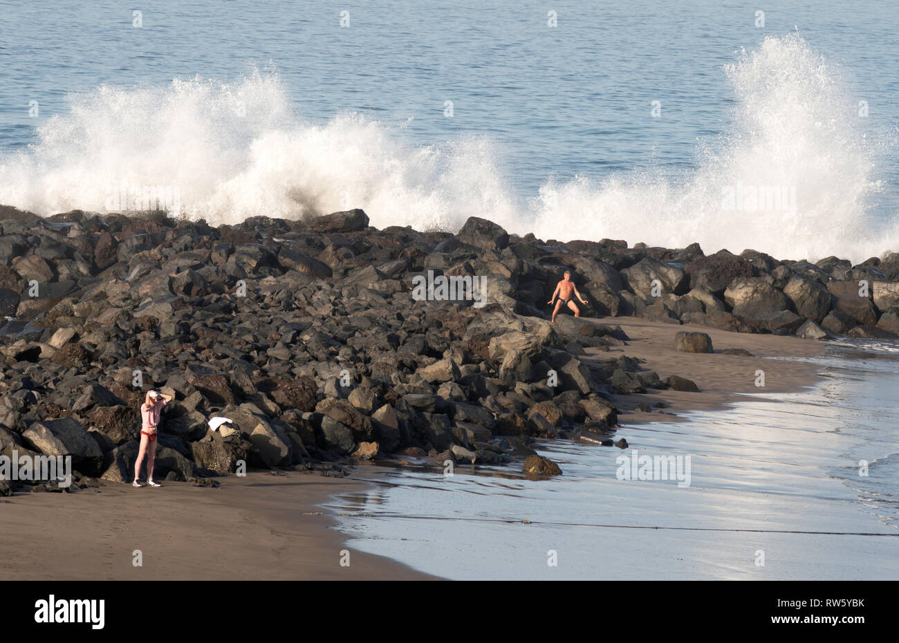 Les personnes exerçant sur la plage tandis que les vagues déferlent dans les rochers derrière, Costa Adeje, Tenerife, Canaries. Banque D'Images