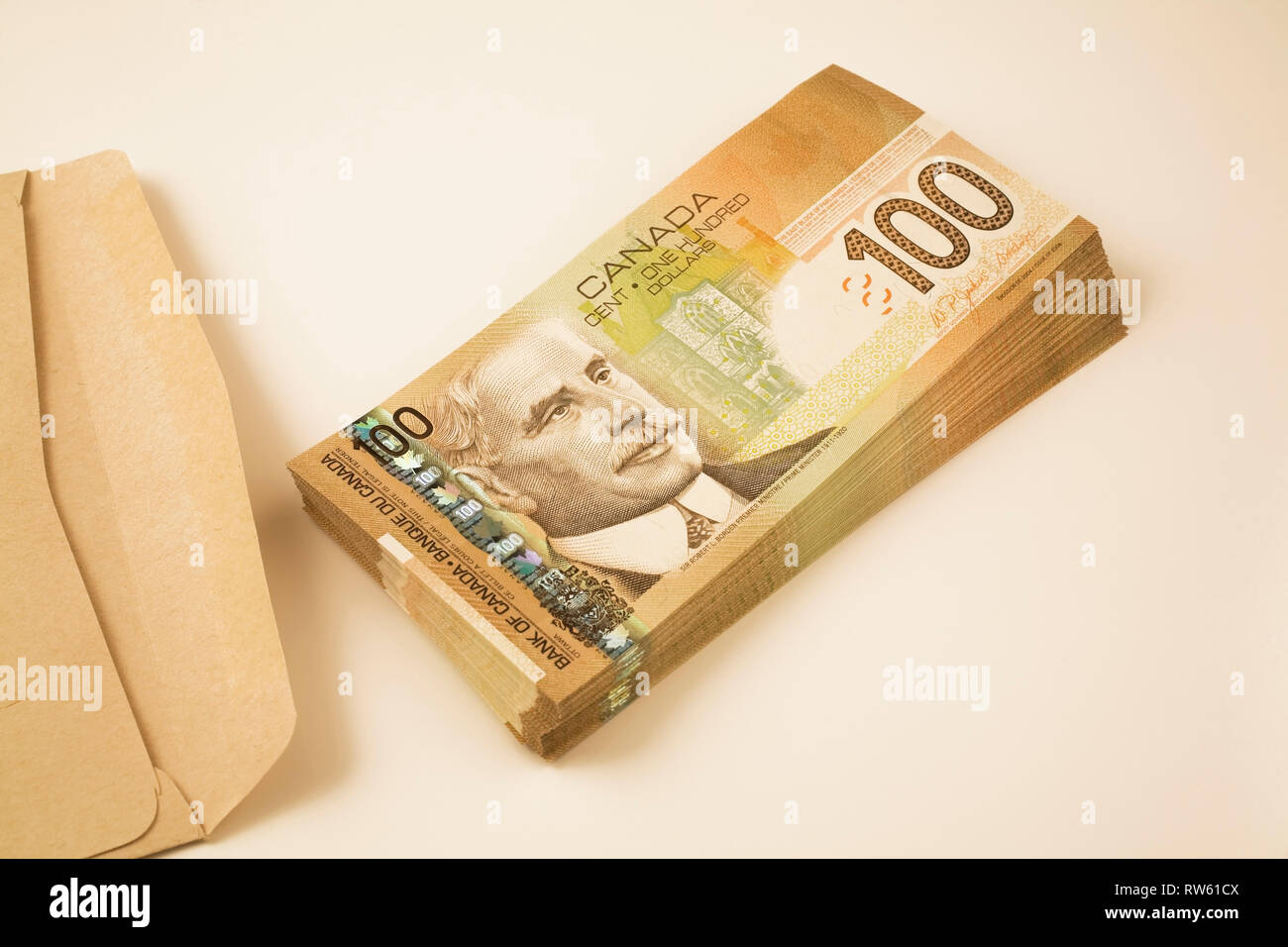 Enveloppe de papier brun à côté d'une pile de dix-mille dollars dans les cent billets de papier-monnaie dollar sur fond blanc Banque D'Images