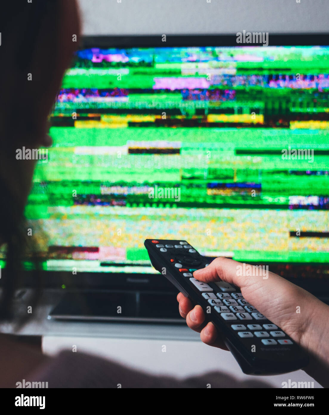 Vertical image woman holding remote control à la recherche au mauvais signal bruit statique de son écran de télévision TVN numérique Banque D'Images