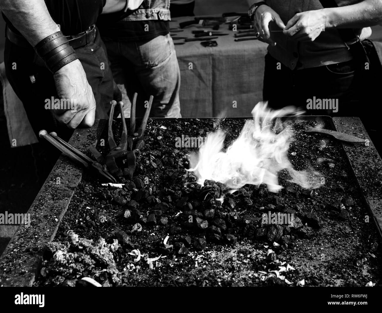 Feu et flammes au lieu de travail du forgeron avec sa main près de la cuisinière de discuter avec le client - noir et blanc Banque D'Images