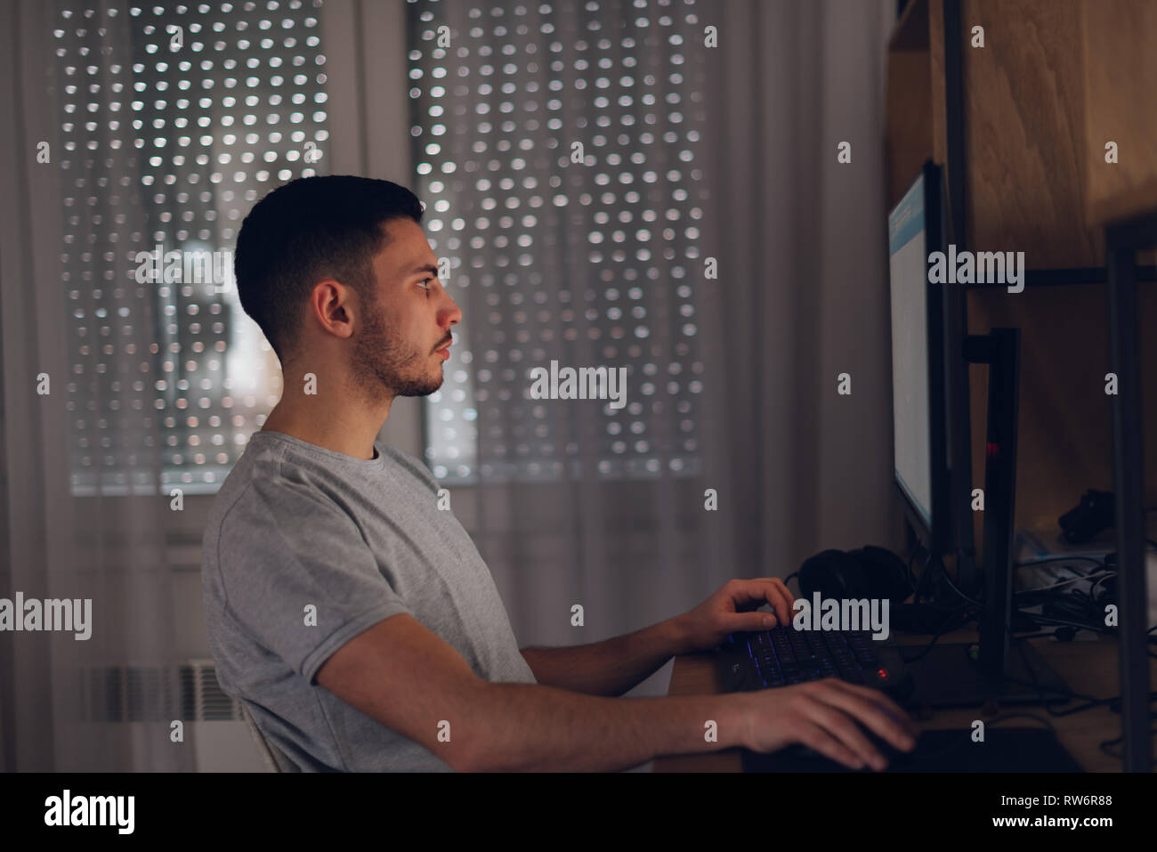 Programmeur travaille sur son ordinateur lorsque l'écran reflète la lumière sur son visage. Banque D'Images
