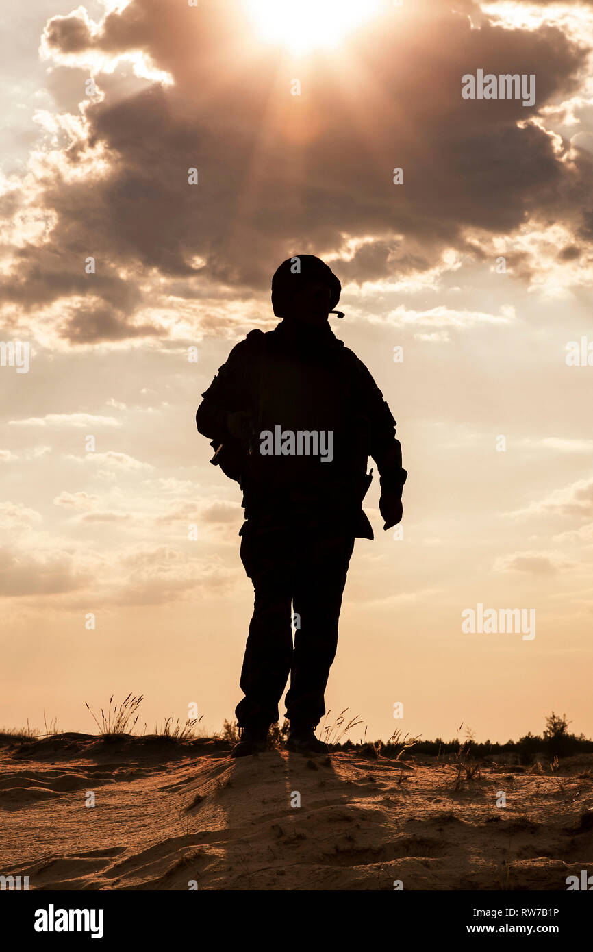 Silhouette de jeune soldat au casque militaire contre le soleil. Banque D'Images