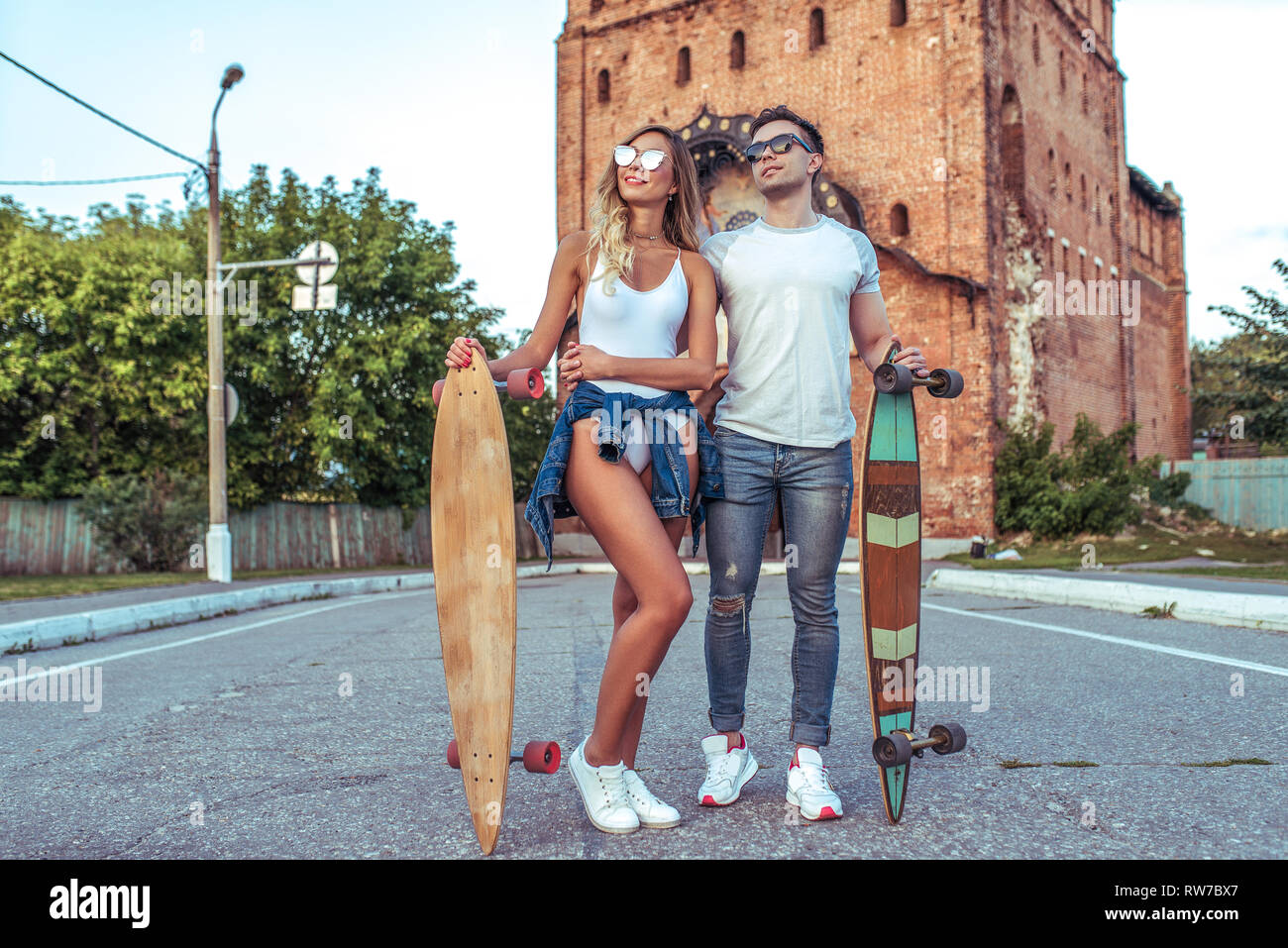 Jeune couple de gars avec une jeune fille sur la route dans les mains de longboard skates. Happy smiling et lunettes de soleil, l'été dans la ville. Sports Concept Banque D'Images