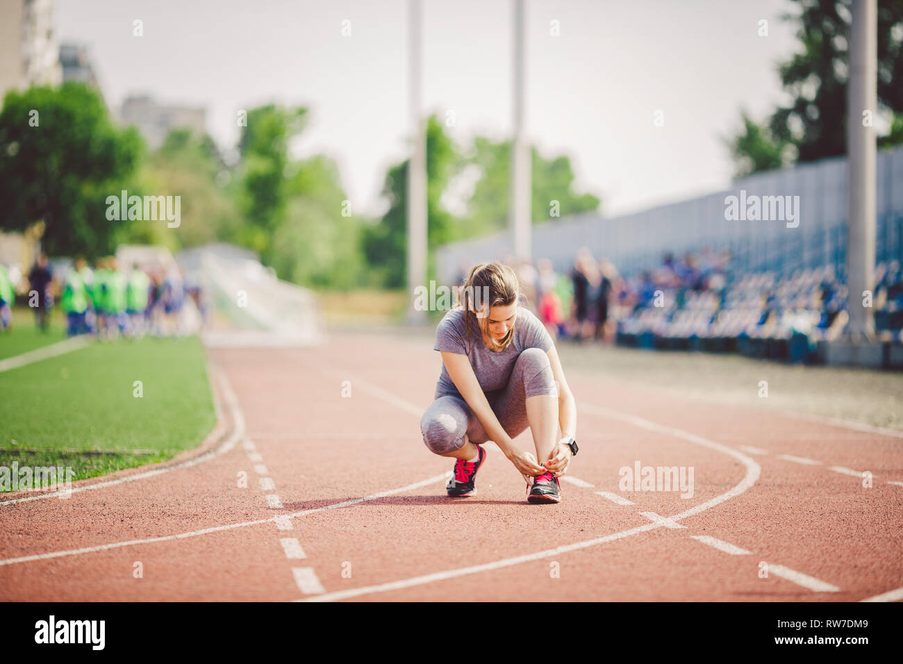 Thème les sports et sportswear. Une jeune femme de race blanche en uniforme le laçage des lacets de chaussures sport réglage de voie sur un tapis roulant dans un stade. Banque D'Images