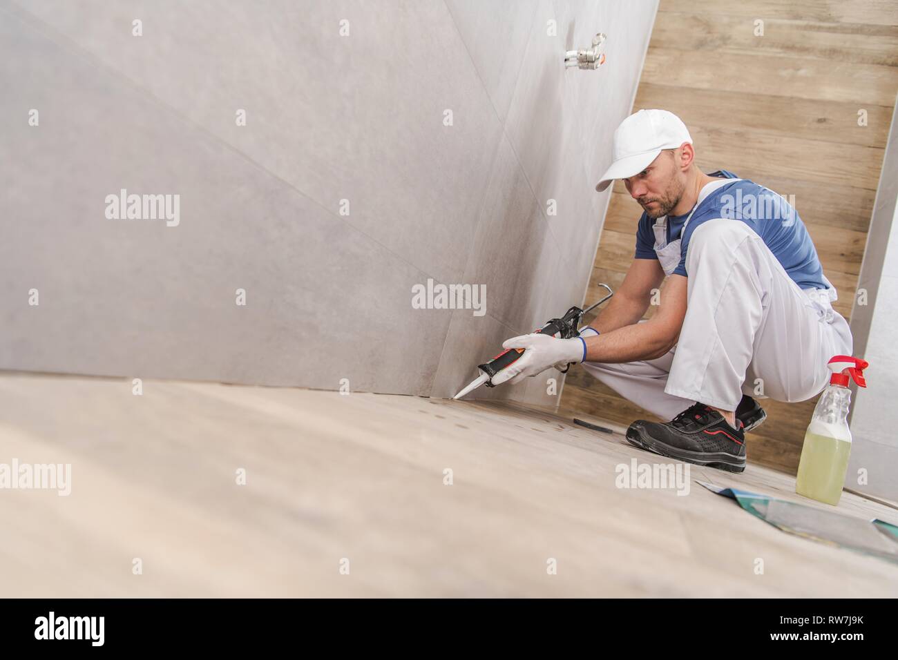 Caucasian Worker dans la trentaine Mur d'étanchéité coins de carreaux de céramique à l'Intérieur de salle de bains récemment rénovée. À l'aide d'un joint en silicone. Banque D'Images