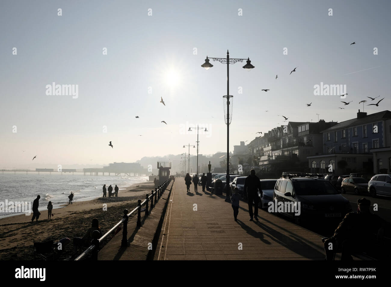 Un dimanche, promenade le long du front de mer et port de Sandown, Isle of Wight, Angleterre, comme les mouettes troupeau au-dessus de la vague lumineuse du soleil d'hiver. Banque D'Images
