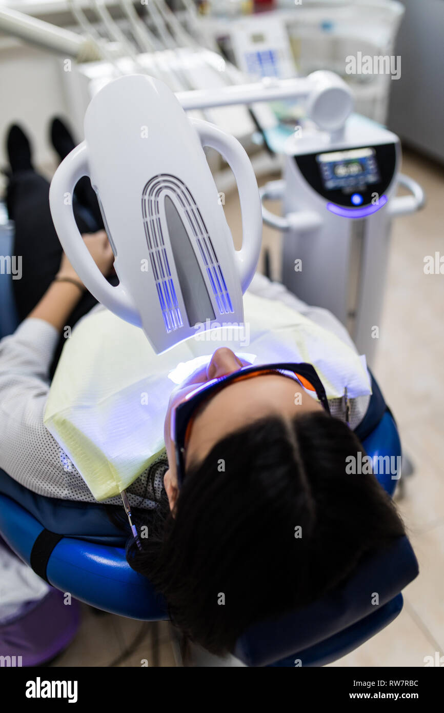 Patient avec des lunettes de sécurité et de l'enrouleur sur la joue. Lampe lumière laser activer comme une procédure de blanchiment des dents professionnels. Women's Cosmet Banque D'Images Patient avec des lunettes de sécurité et de l'enrouleur sur la joue. Lampe lumière laser activer comme une procédure de blanchiment des dents professionnels. Women's Cosmet Banque D'Images