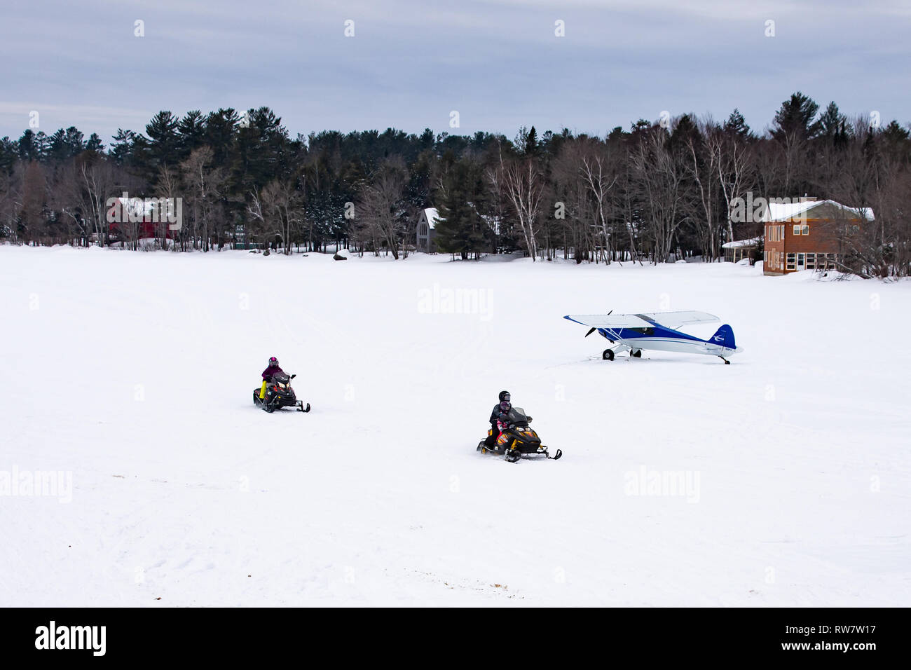 Deux motoneiges traversant le lac Pleasant dans les Adirondacks, NY USA passé un Cub Crafters aéronefs expérimentaux sur des skis en stationnement sur la glace. Banque D'Images