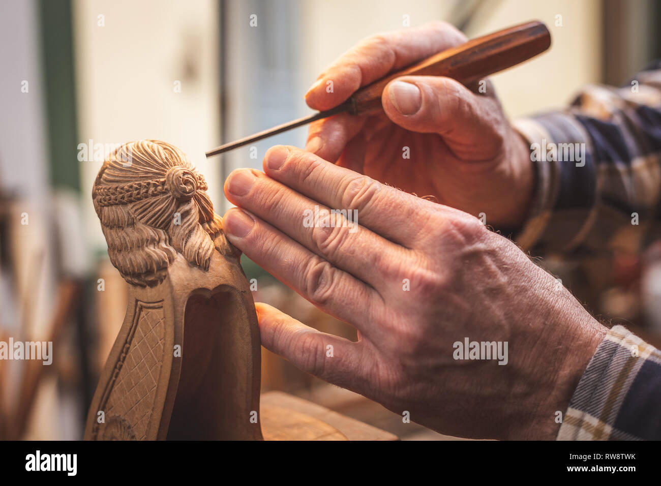 Mains d'un sculpteur sur bois à l'aide d'un outil travaillant sur une petite figure en bois Banque D'Images