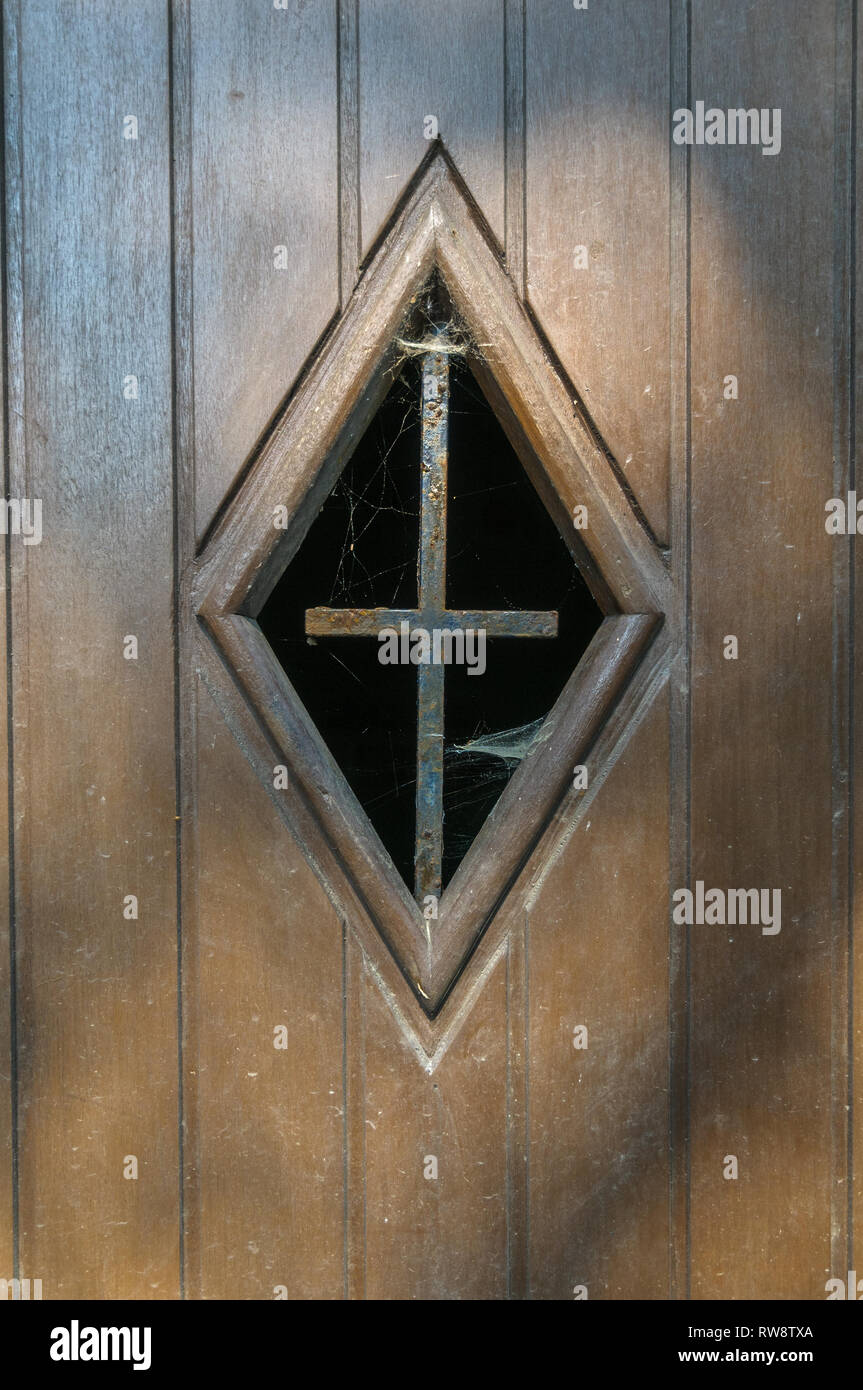 Gros plan d'une fenêtre dans une porte en bois d'une ancienne chapelle routière près de La Roche-en-Ardenne en Belgique. Dans la fenêtre il y a une vieille croix de fer rouillée wi Banque D'Images