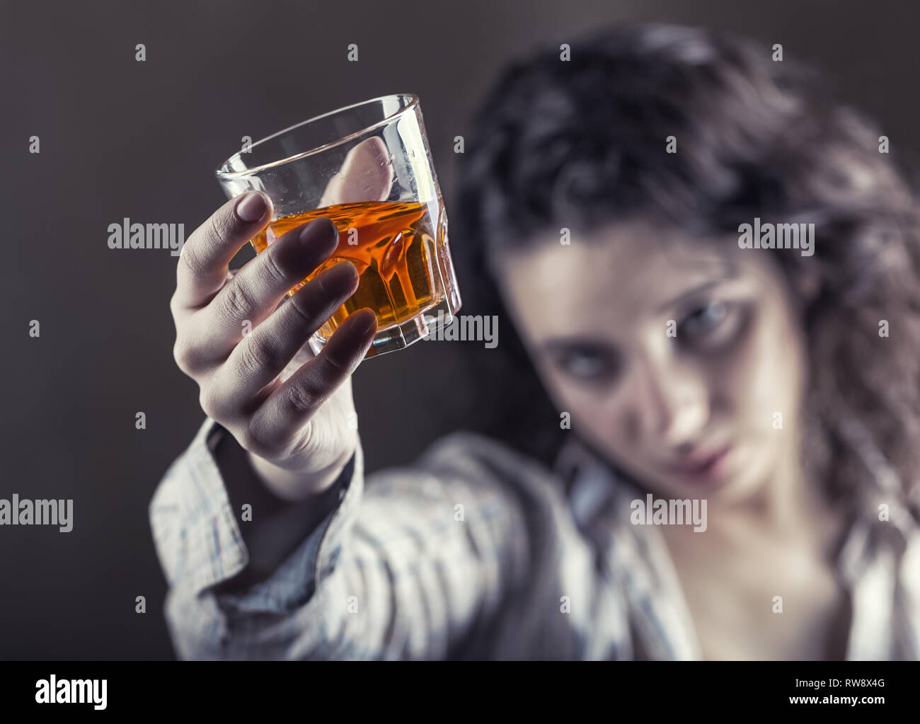 Jeune femme dans la dépression, boire de l'alcool sur fond sombre. Se concentrer sur le verre Banque D'Images