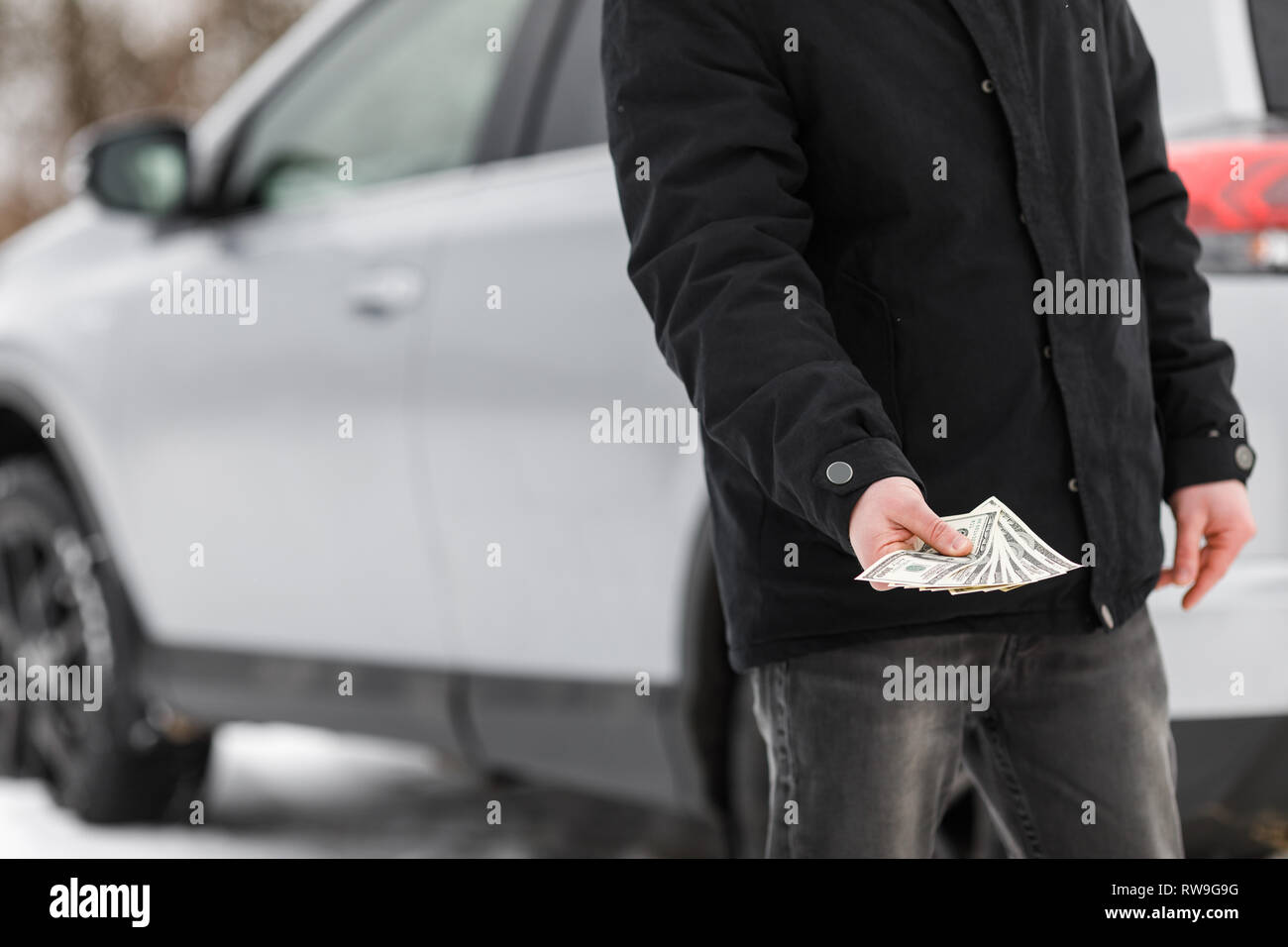 L'homme avec de l'argent près de voiture. Dollars de l'argent dans le réservoir de carburant de voiture. Banque D'Images