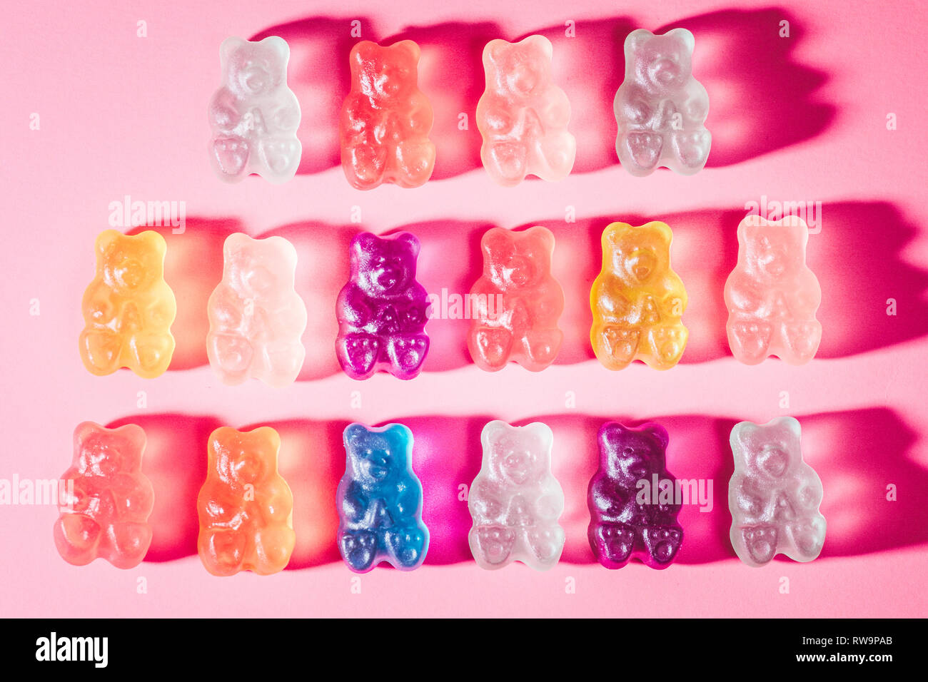 Un close-up de trois rangées d'ours gommeux vivement colorées, photographié sur un fond rose avec poppy studio light. Banque D'Images