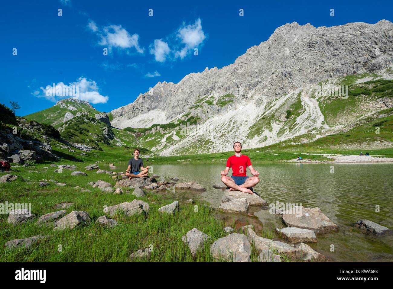 Deux jeunes gens assis sur des pierres et méditer, lac de montagne à l'Prinz-Luitpold-House, Alpes d'Allgäu, Bad Hindelang, Allgäu Banque D'Images