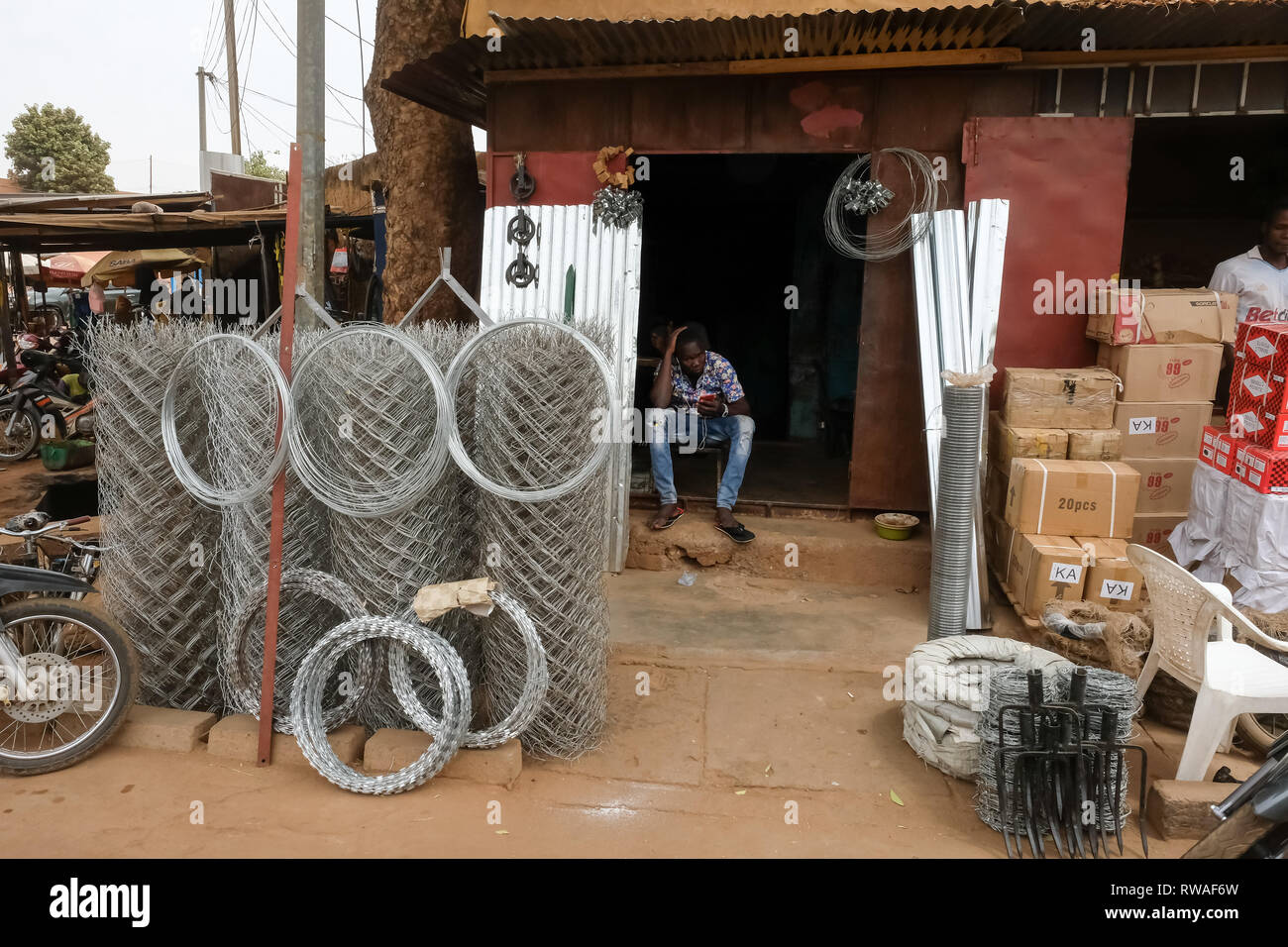 La petite entreprise en Afrique : un homme est assis à un petit commerce de vente de fil de clôture d'acier et d'autres produits métalliques au Burkina Faso, Afrique de l'ouest Banque D'Images
