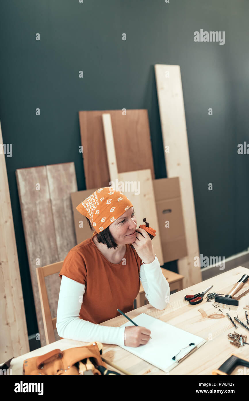 Female carpenter est de boire du café et de la planification projet de bricolage dans sa petite entreprise atelier de menuiserie Banque D'Images