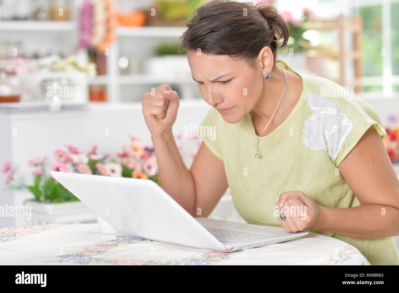 Portrait de angry young woman using laptop in kitchen Banque D'Images