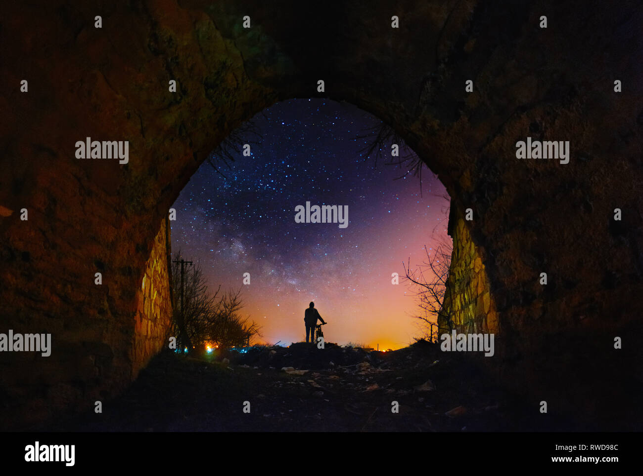 Un gars avec location d'un séjour sous le pont arc et regarder dans le ciel nocturne et Milky Way. Paysage pittoresque rural l'astrophotographie. Banque D'Images
