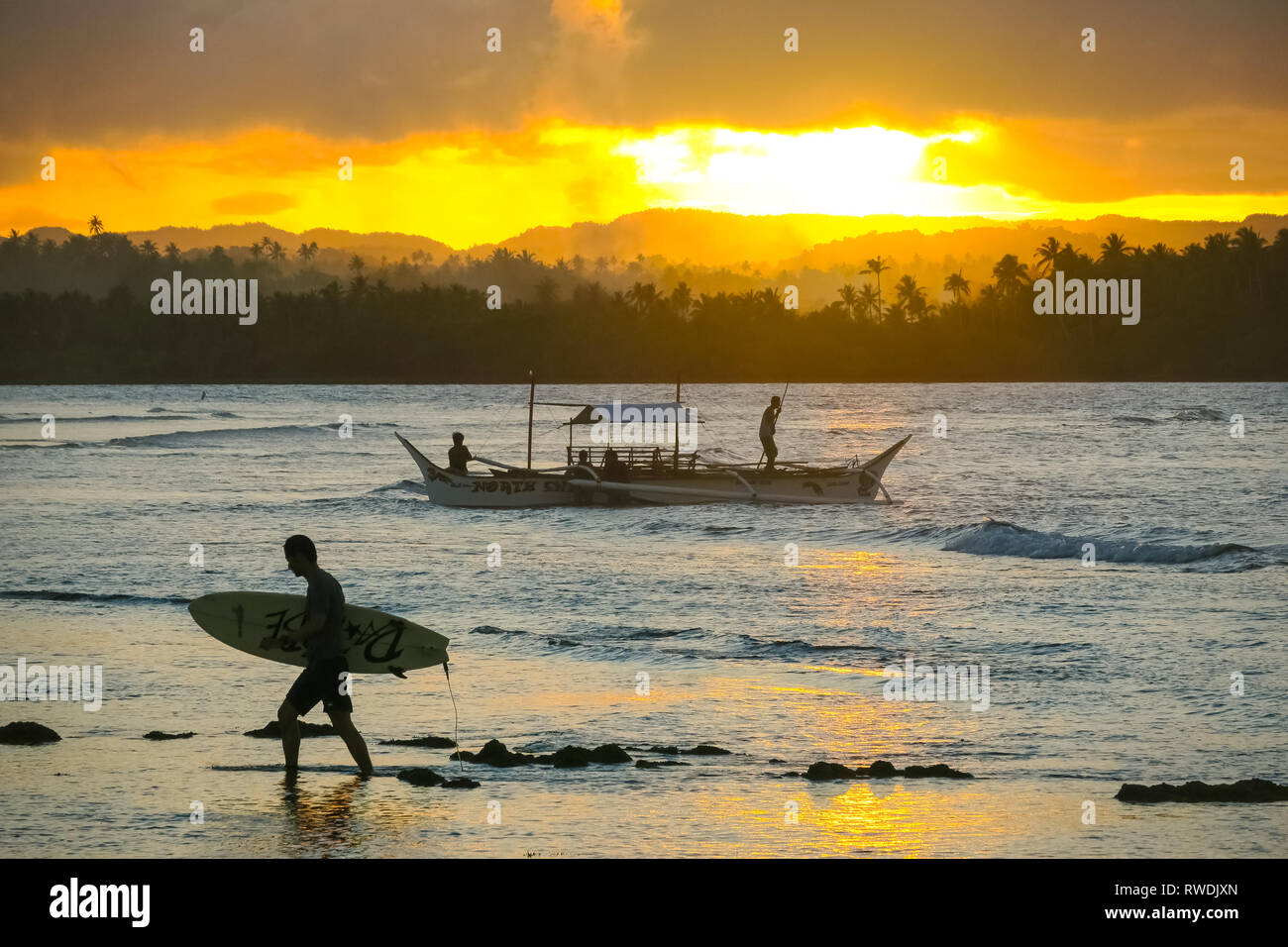 Surfer avec une planche de surf, randonnée pédestre sur plage avec Excursion en bateau et coucher de soleil à distance - Cloud 9 - Siargao, Philippines Banque D'Images