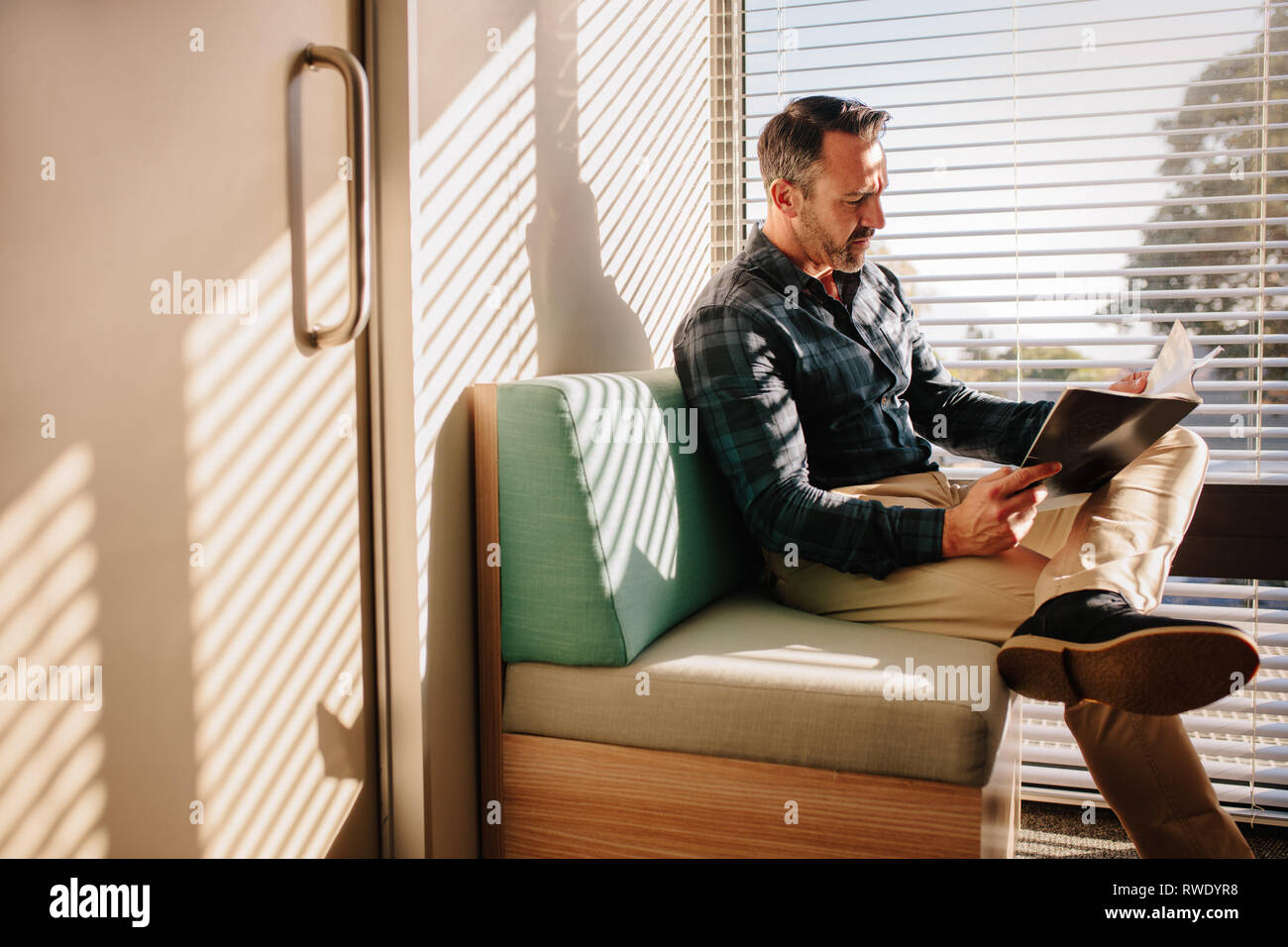 Les patients de sexe masculin en lisant un livre dans la salle d'attente du médecin. Patient de sexe masculin à la réception d'une clinique, assis sur un canapé avec un livre. Banque D'Images