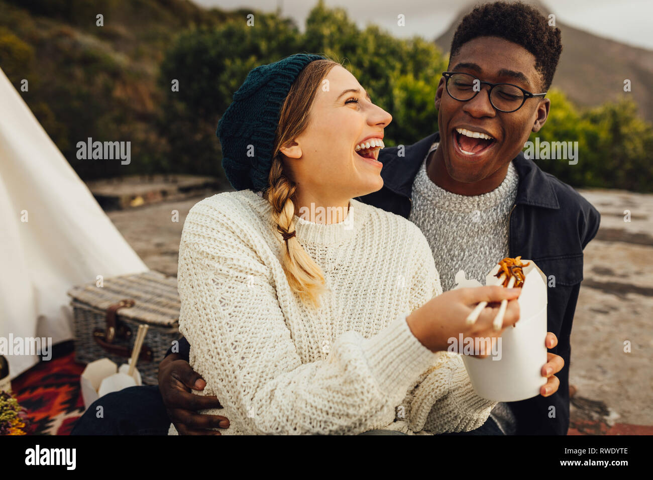 L'Interracial couple outdoors on picnic. Alimentation Alimentation femme à son petit ami alors qu'il était assis à l'extérieur. Banque D'Images