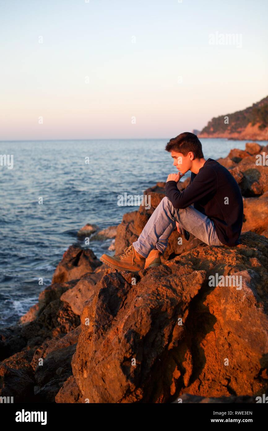 Beau garçon regardant la mer au coucher du soleil, Lluc Alcari, Deia, Mallorca Espagne Banque D'Images