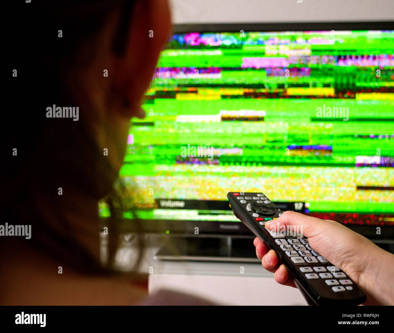 Vue arrière du woman holding remote control à la recherche au mauvais signal du bruit statique provenant de ses téléviseurs écran plat numérique DTV distorsions de réception du signal . Banque D'Images