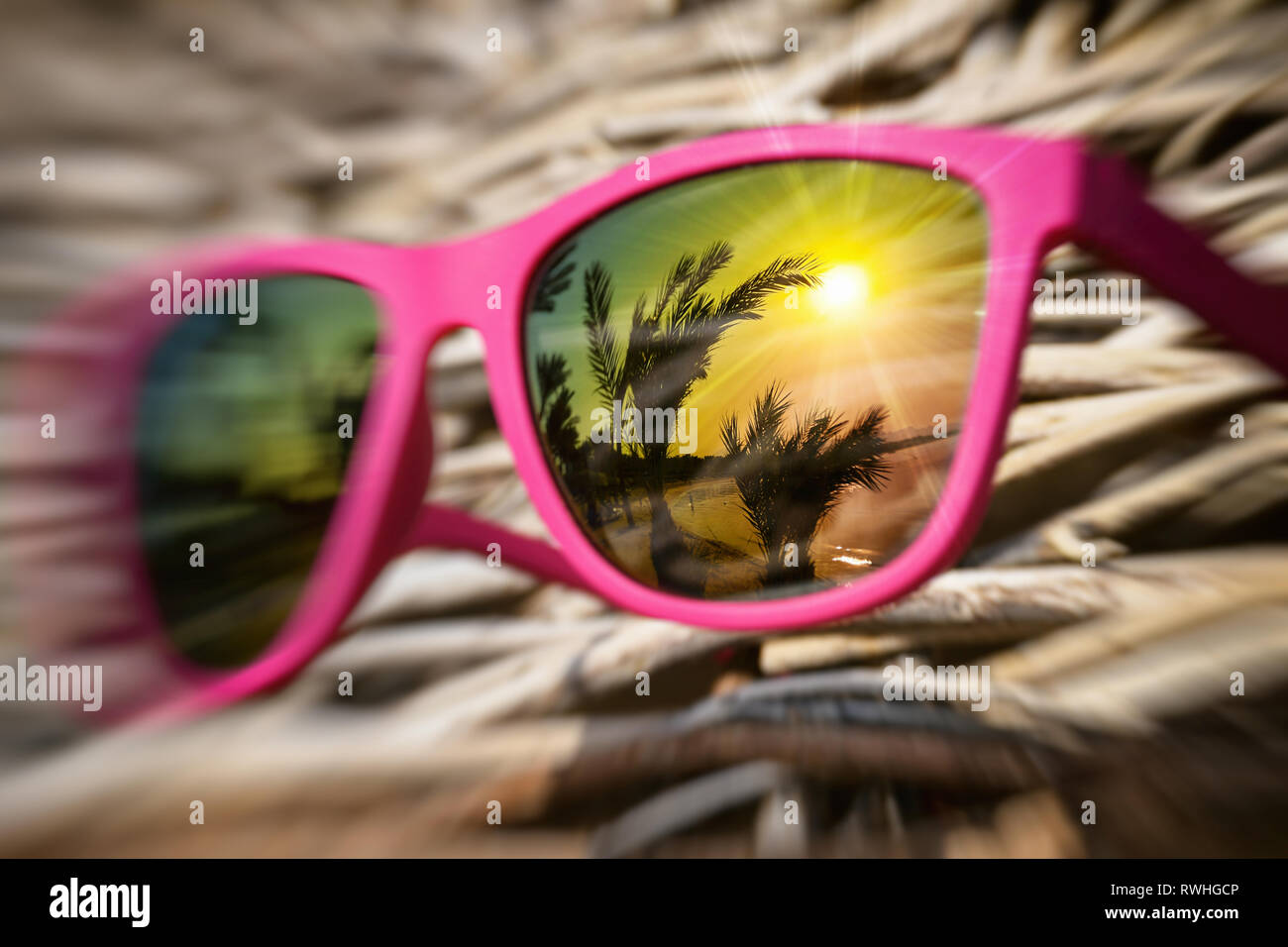 Lunettes de soleil rose élégante sur un cadre en bois avec de beaux reflet  dans le verre coloré de la plage avec des palmiers et le coucher du soleil  Photo Stock -