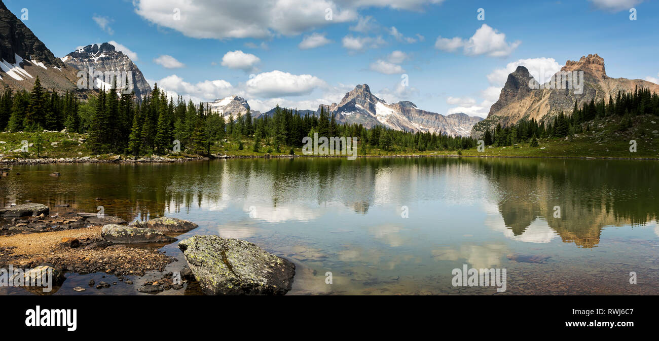 Gamme de montagne la réflexion sur un lac alpin avec un rivage rocailleux et ciel bleu et nuages ; British Columbia, Canada Banque D'Images