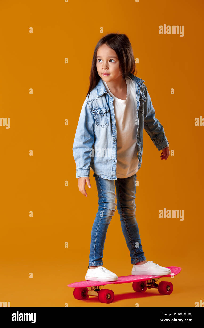 Petit enfant fille elegante avec des vetements en jeans de skate sur fond orange Photo Stock Alamy