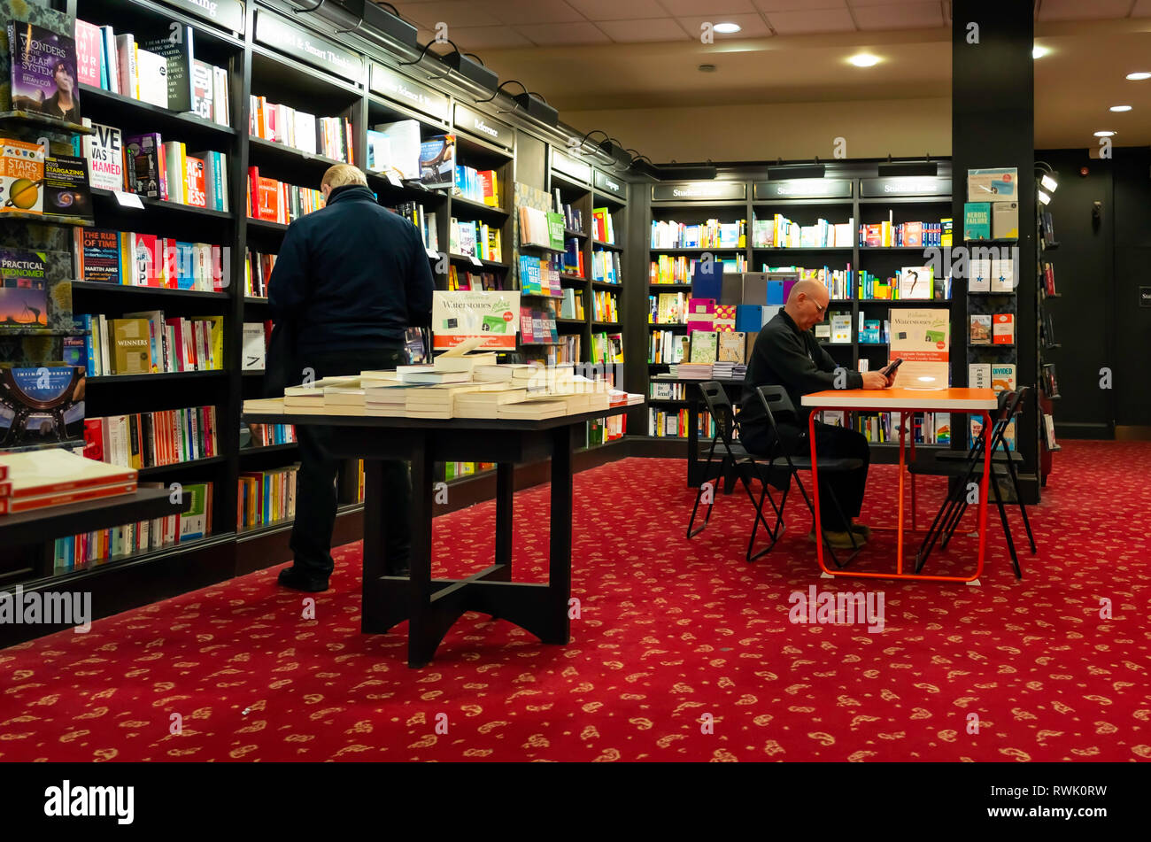 Deux hommes dans une librairie une seule lecture à une table et l'autre parcourant les étagères Banque D'Images
