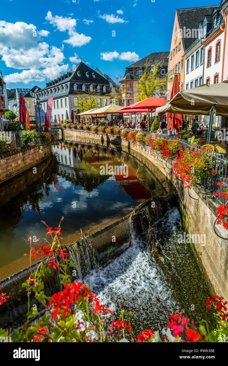 Canal avec chutes d'eau en village coloré avec des jardinières de fleurs le long de rampes et ciel bleu avec des nuages, Saarburg, Allemagne Banque D'Images