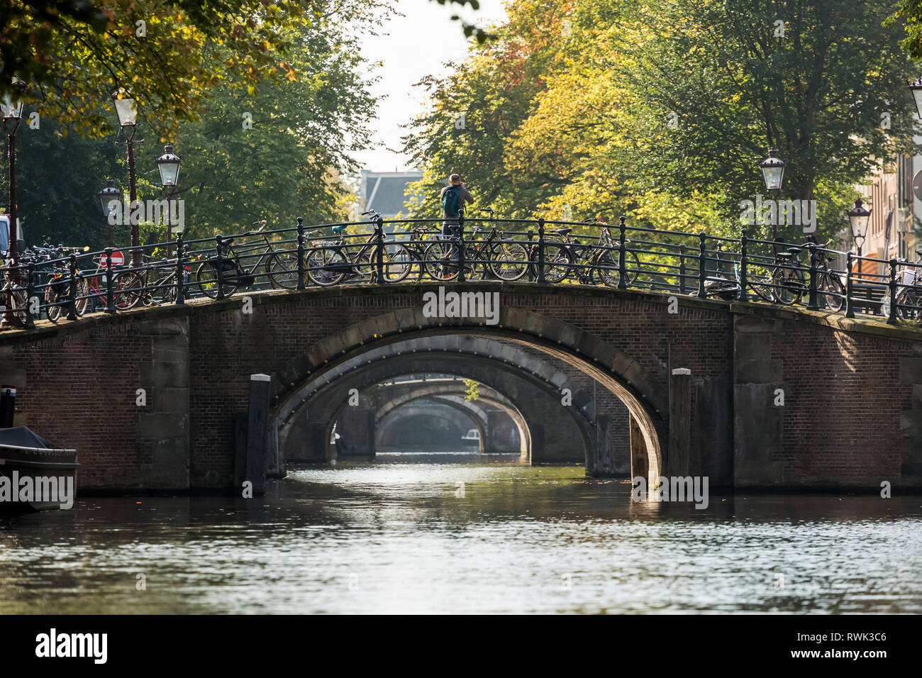 Plusieurs moyens de passage de pont en pierre le long d'un canal avec plusieurs motos sur main courante ; Amsterdam, Pays-Bas Banque D'Images