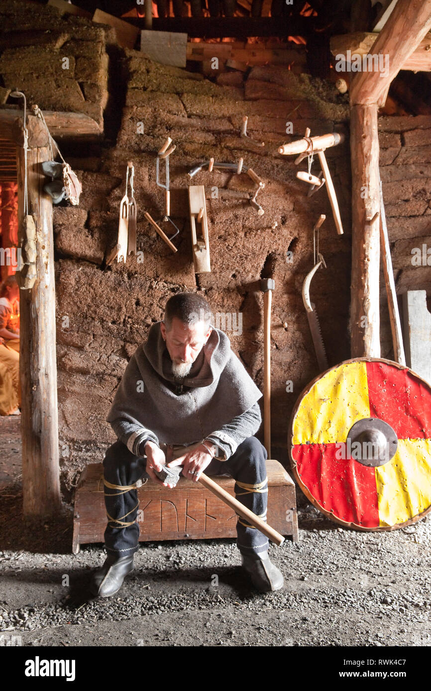 Parcs Canada intepreter en costume d'une hache d'affûtage à l'abri dans une maison longue Viking à L'Anse aux Meadows National Historic Site, L'Anse aux Meadows, Terre-Neuve, Canada Banque D'Images