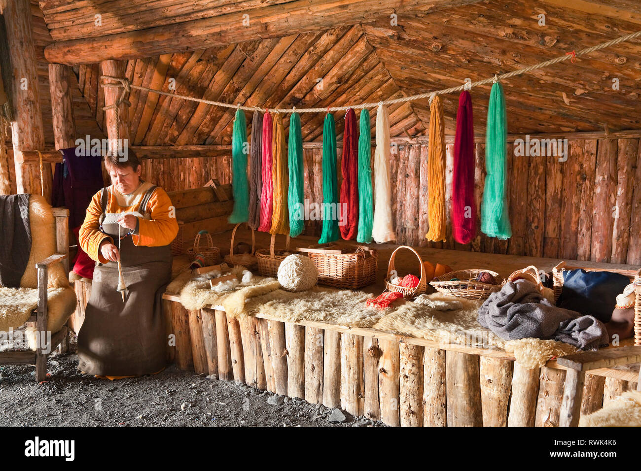 Reenactor en costume entouré par des fils de couleurs différentes et de filage d'une longueur de fil à l'aide d'une liste déroulante fuseau, Norstead Village Viking et le port de commerce, DE L'Anse aux Meadows, Terre-Neuve, Canada Banque D'Images