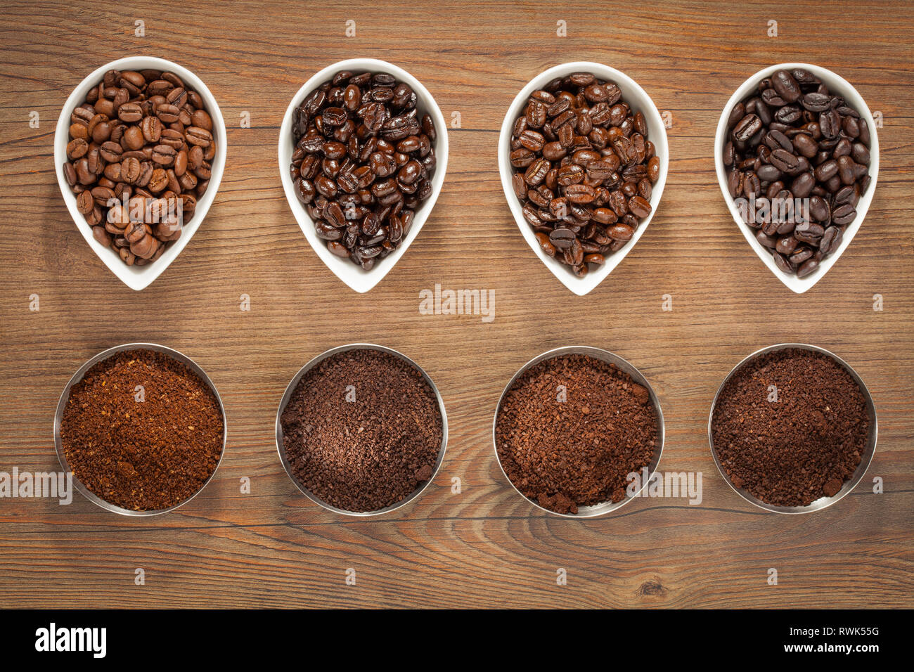 Vue de dessus de quatre variétés de fèves de café torréfié avec leurs homologues fraîchement moulu dans de petits bols sur un fond en bois brun Banque D'Images