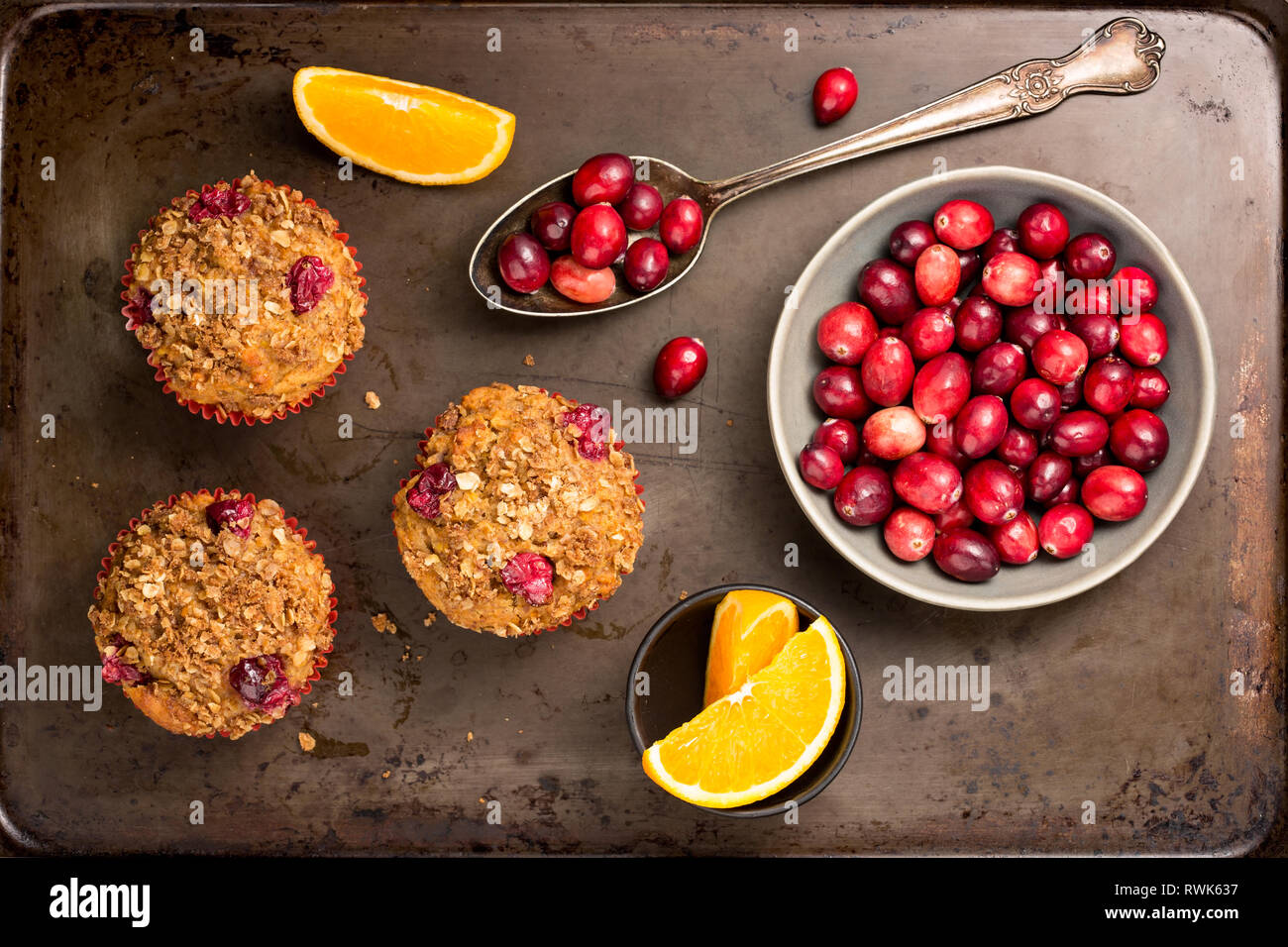 Muffins aux canneberges fraîchement cuits sur un plat de cuisson rustique avec des canneberges et des tranches d'orange. Banque D'Images