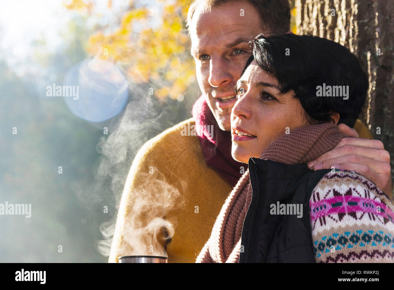 Couple having boisson chaude à côté de tree Banque D'Images