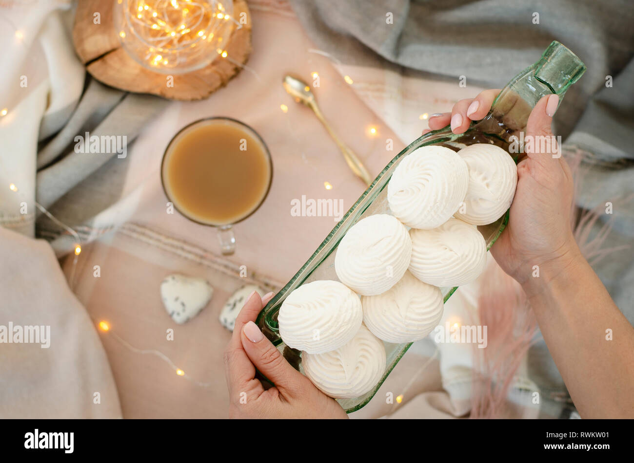 Les mains tenant un plat de service transparent blanc avec des meringues. Concept de dessert. Banque D'Images