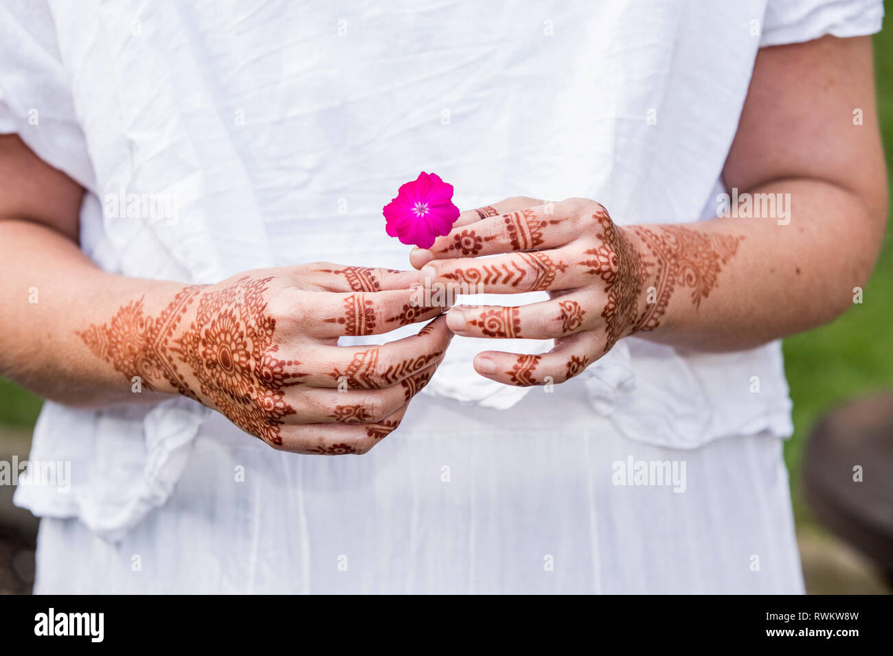 Femme en robe blanche avec tatouage au henné sur les mains holding flower Banque D'Images