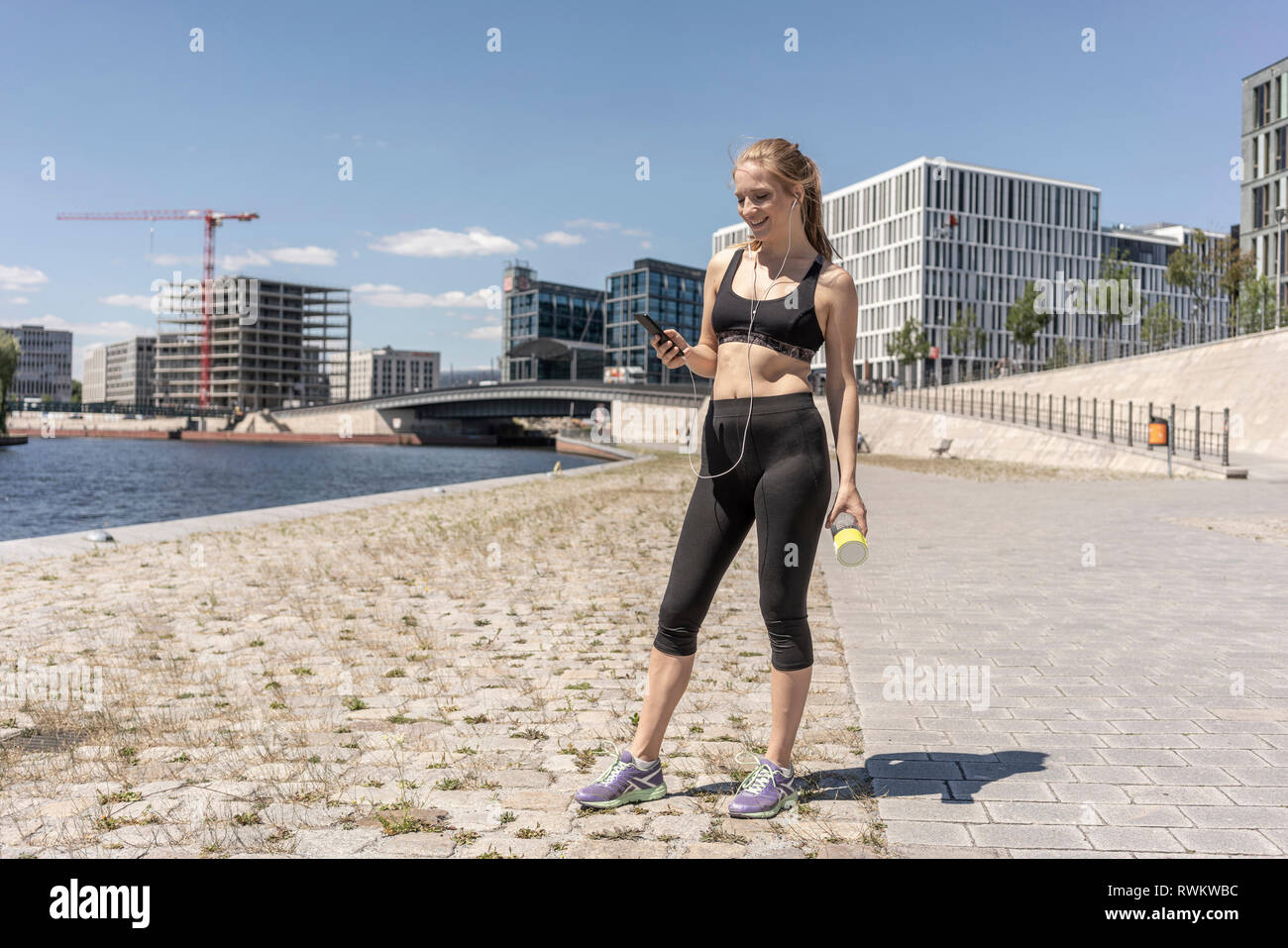 Jeune femme en rupture avec l'exercice et de l'utilisation de smartphone dans ville, Berlin, Allemagne Banque D'Images
