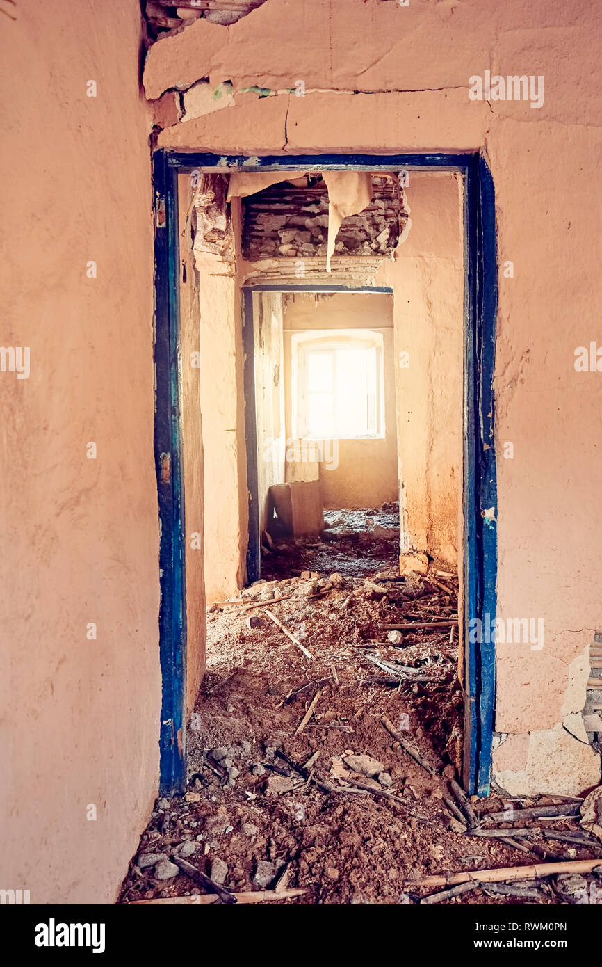 Intérieur d'une ancienne maison rurale désolé rose clair avec des murs lézardés, détachée et porte un plancher couvert de boue et de broussailles. Banque D'Images