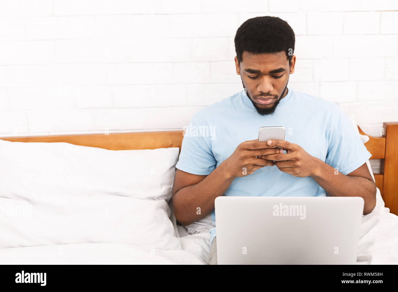 Jeune homme en pyjama using cellphone in bed Banque D'Images