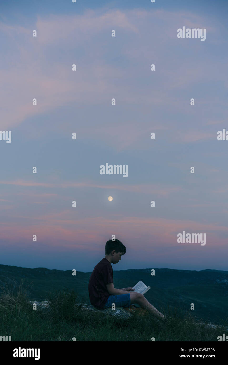 Boy reading book on hilltop, Snowdonia, Llanberis, Gwynedd, UK Banque D'Images