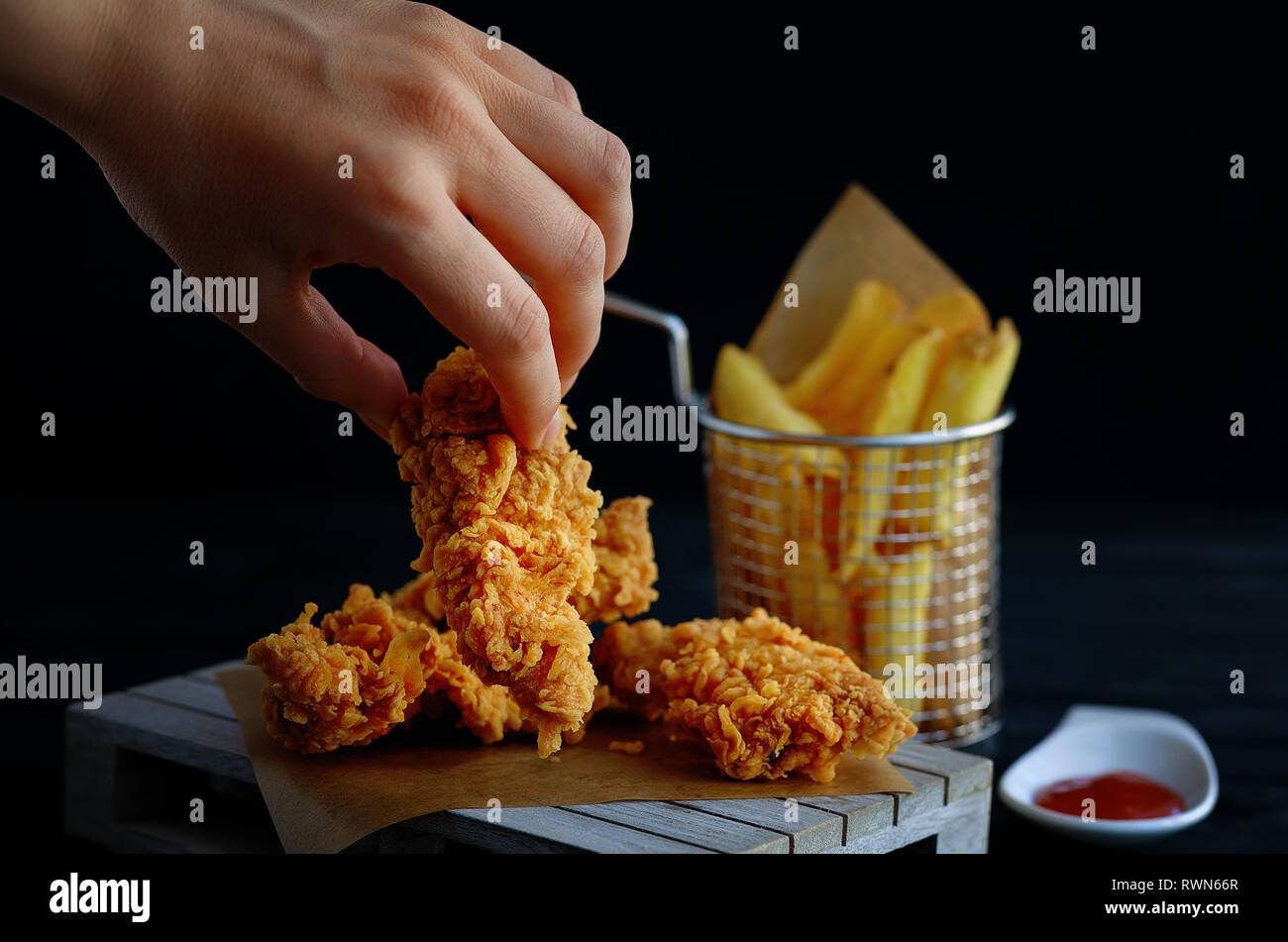 Main saisit croustillant de Kentucky Fried Chicken de frites et de tomates sur table en bois noir Banque D'Images