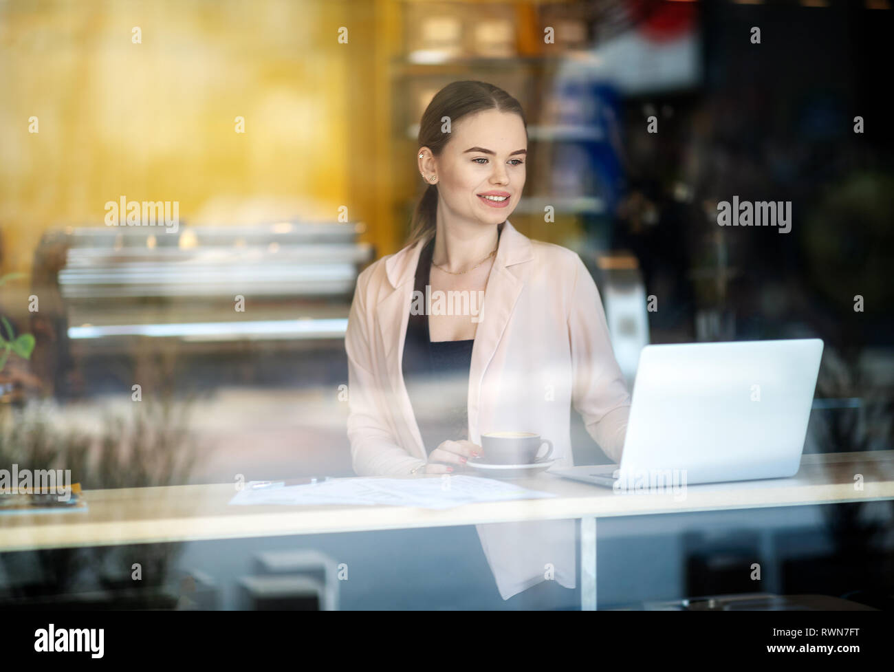 Smiling Woman working on laptop at coffee shop. Réflexions de la fenêtre. Shot of a young woman using a laptop in a cafe Banque D'Images