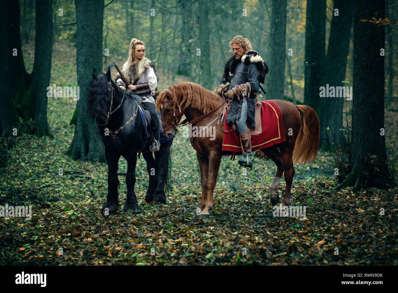 Un homme sur femme guerriers chevaux dans les bois. Les vikings scandinaves équitation avec des haches dans les mains. Vêtements traditionnels à col fourré. Reconstructio Banque D'Images
