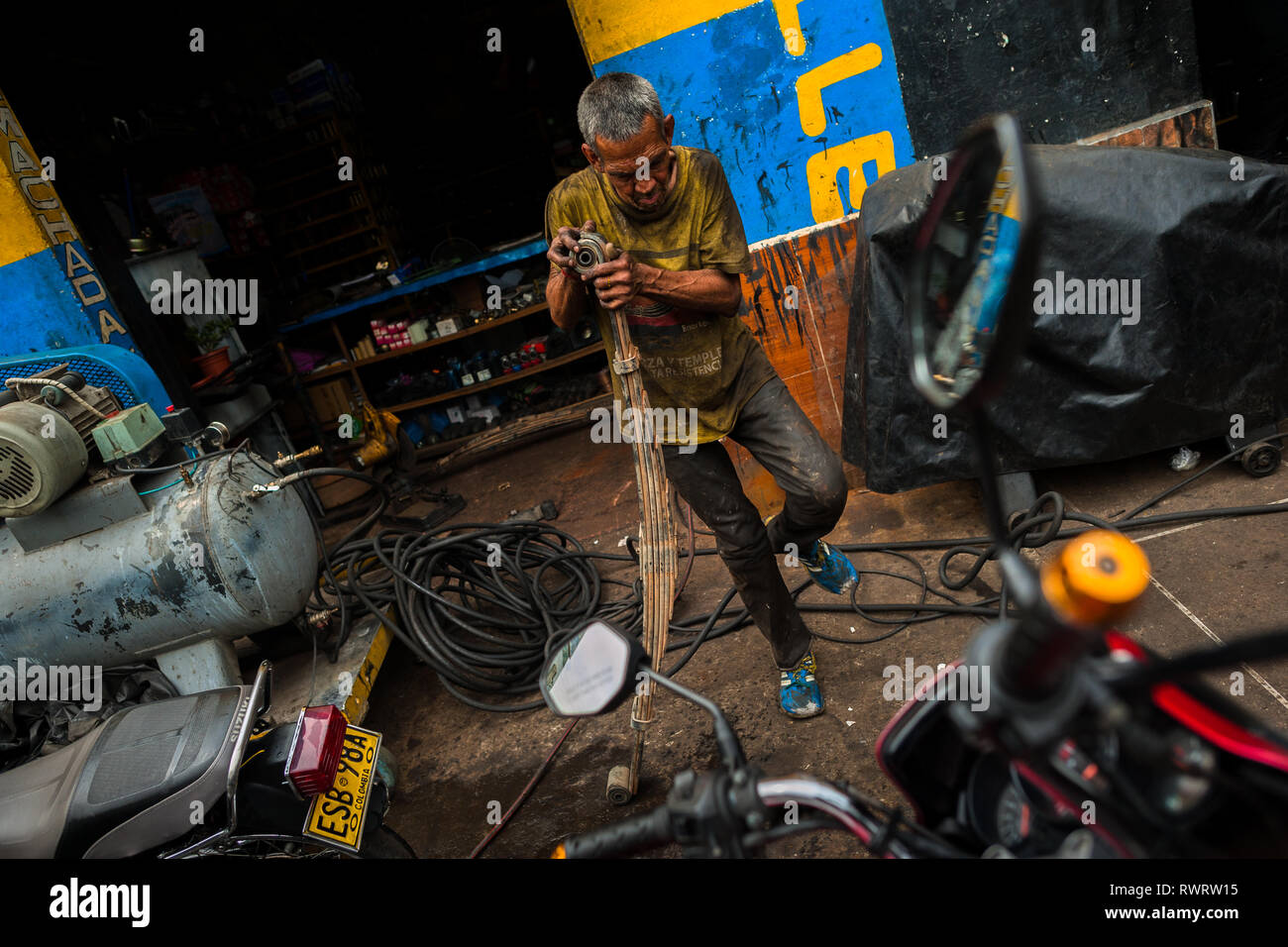 Un mécanicien de voiture fonctionne sur le camion des ressorts à lames dans un atelier de réparation de voiture dans le Barrio Triste, Medellín, Colombie. Banque D'Images