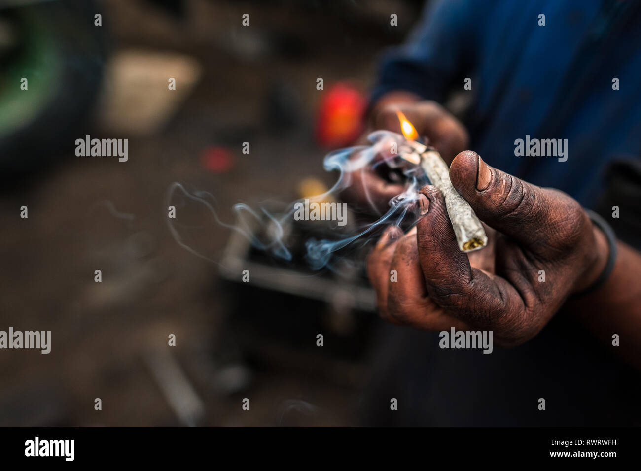 Un mécanicien de voiture s'allume une cigarette de marijuana lors d'une courte pause de travail dans Barrio Triste, Medellín, Colombie. Banque D'Images